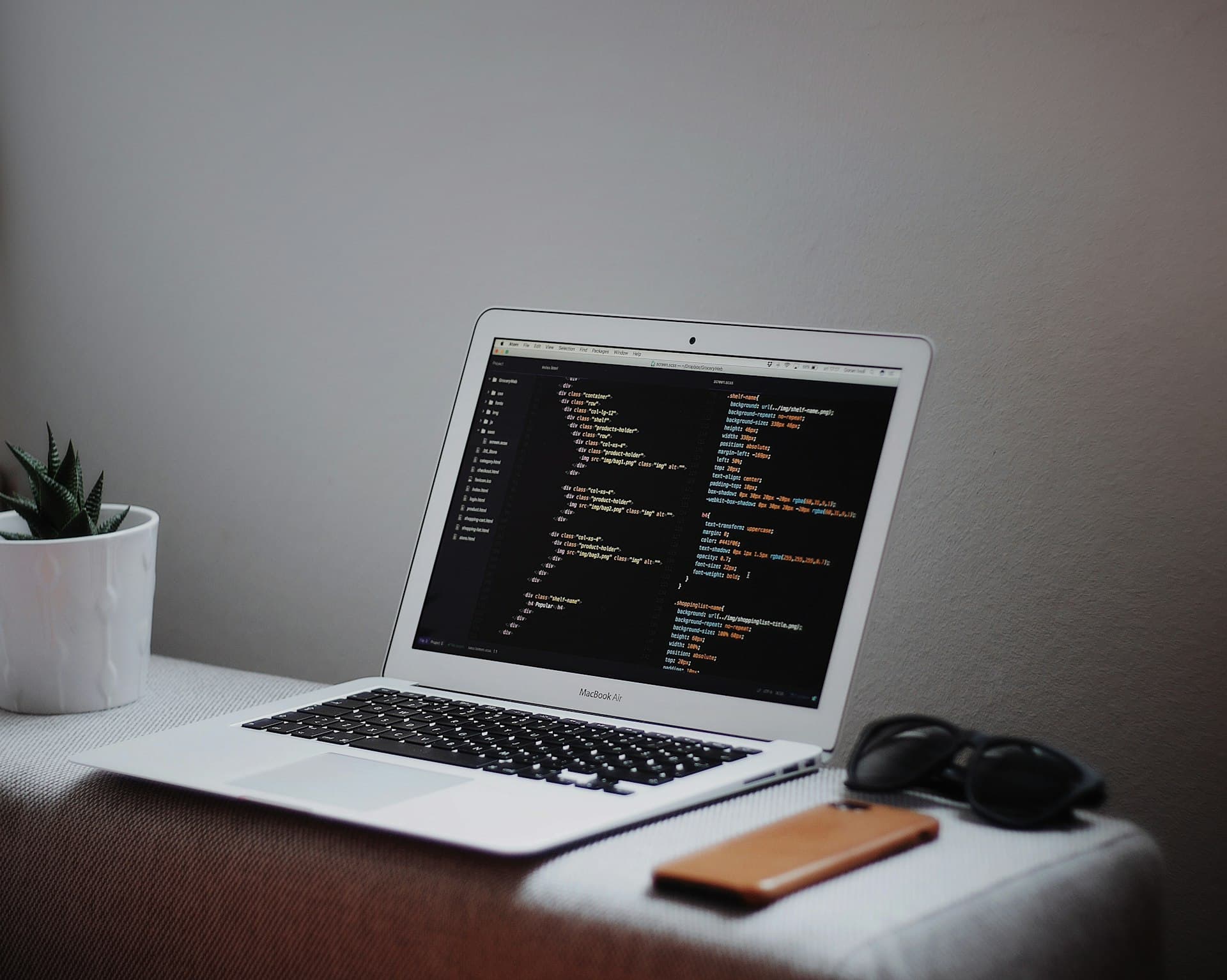 لابتوب على مكتب بيعرض كود HTML و CSS في محرر أكواد، جنبه نبتة صغيرة ونضارة شمس