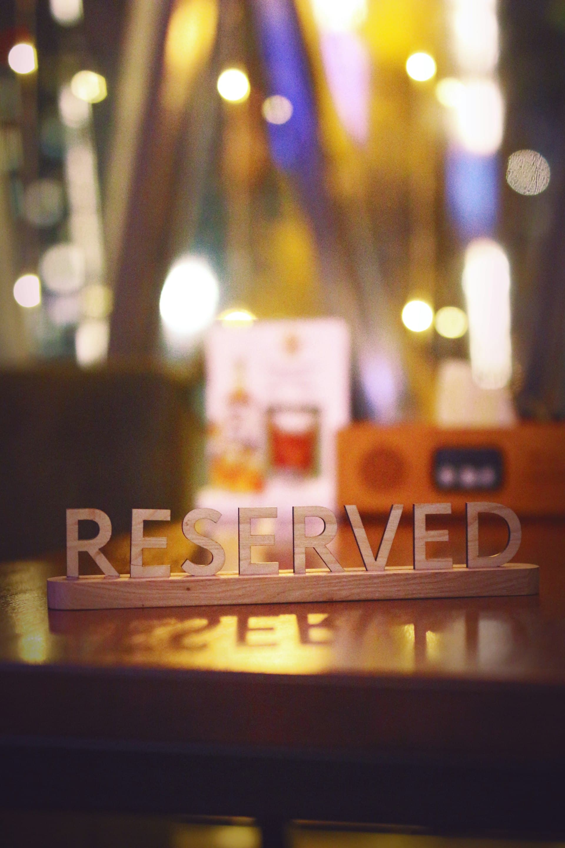 حروف خشب مكتوب عليها RESERVED واقفة على ترابيزة مطعم وإضاءة دافية معلقة في الخلفية غير واضحة