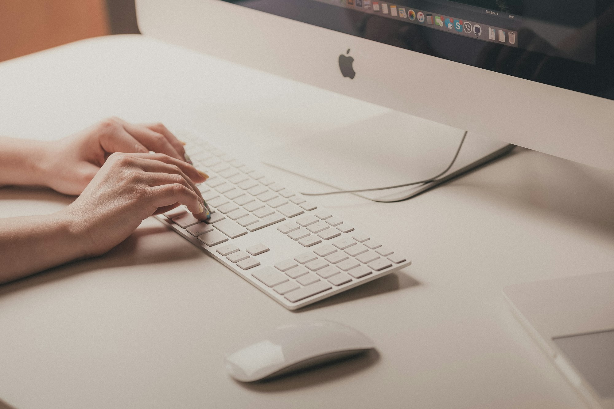لقطة قريبة لإيدين بيكتبوا على كيبورد قدام شاشة iMac